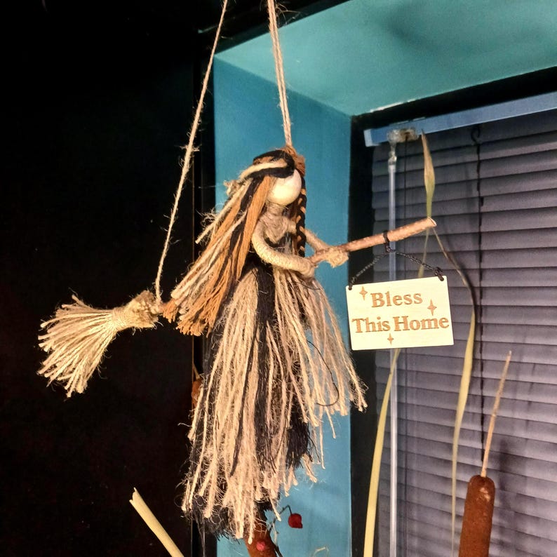 May include: A handmade witch doll with a broom, crafted from natural twine and rope. The doll has long, flowing hair and a black and beige dress. A small wooden sign reads "Bless This Home".