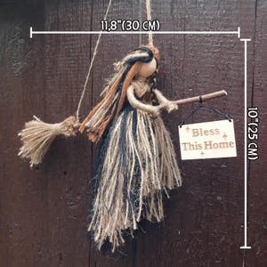 May include: A handcrafted witch doll, 10 inches (25 cm) tall and 11.8 inches (30 cm) wide, made of natural fibers. The doll holds a broom and a wooden sign that reads "Bless This Home". The witch's dress is black, brown, and beige.
