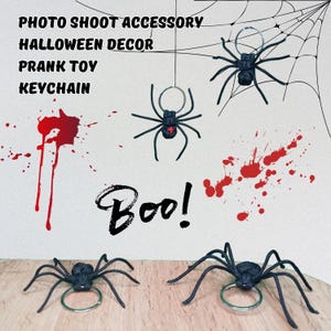 Könnte beinhalten: Schwarze Spinnen-Schlüsselanhänger und Halloween-Dekorationen mit dem Wort "Boo!" in einer gruseligen Schriftart. Das Bild enthält rote Spritzer und ein Spinnennetz-Design. Der Text auf dem Bild lautet "Photo Shoot Accessory, Halloween Decor, Prank Toy, Keychain."