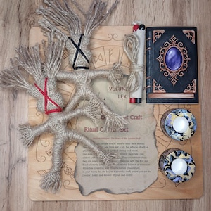 May include: A ritual craft set featuring jute dolls, candles, a book, and a scroll. The dolls have black and red accents. The book has a purple gem on the cover. The set includes a wooden board with text.