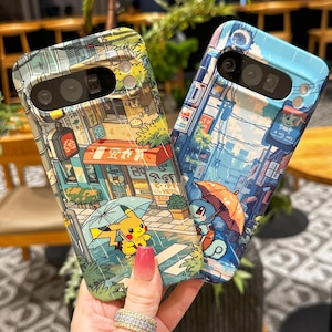 May include: Two phone cases with colorful illustrations. One case features Pikachu under an umbrella in a rainy street scene. The other case shows Squirtle under an umbrella in a similar setting. Both cases have a cityscape design.