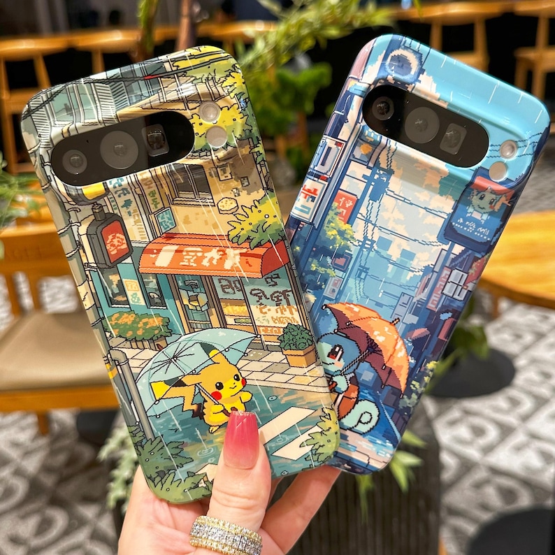 May include: Two phone cases with colorful illustrations. One case features Pikachu under an umbrella in a rainy street scene. The other case shows Squirtle under an umbrella in a similar setting. Both cases have a cityscape design.