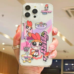 Könnte beinhalten: Transparente Handyhülle mit Powerpuff Girls-Charakteren. Die Hülle hat mehrere Aufkleber mit Blossom, Bubbles und Buttercup. Die Hülle hat ein rosa und lila Farbschema mit den Worten "Powerpuff Girls" und "The Powerpuff Girls".