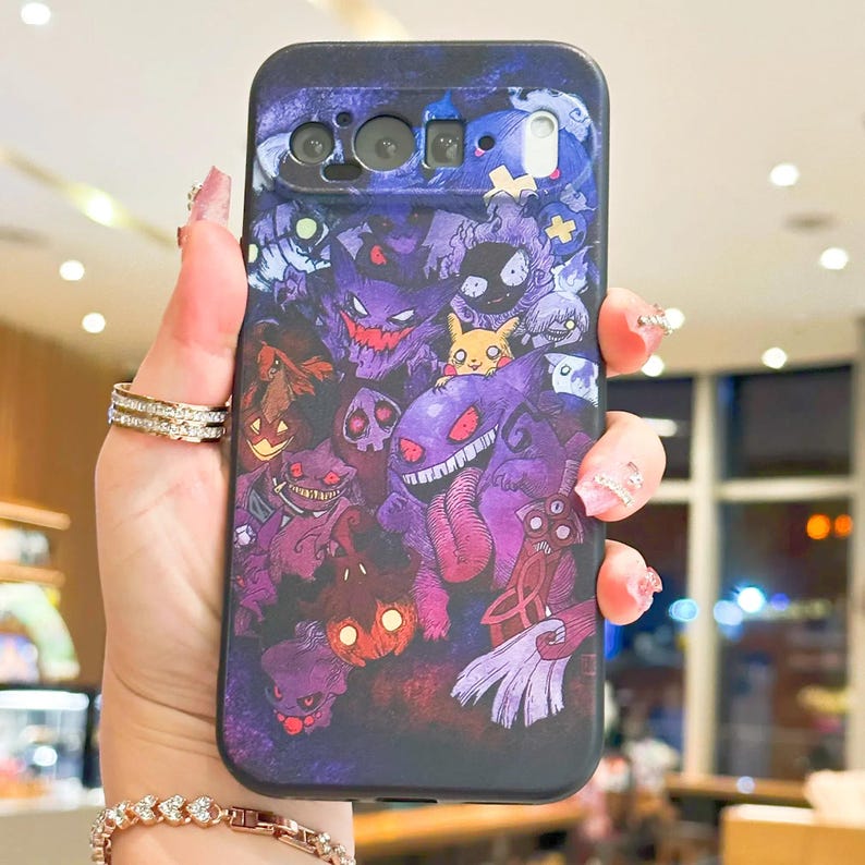 Puede incluir: Una funda de tel&eacute;fono con un dise&ntilde;o colorido de personajes de fantasmas de dibujos animados en tonos morados, rojos y amarillos. La funda tiene un fondo azul oscuro y recortes para la c&aacute;mara y los botones del tel&eacute;fono. El dise&ntilde;o es detallado y llamativo.