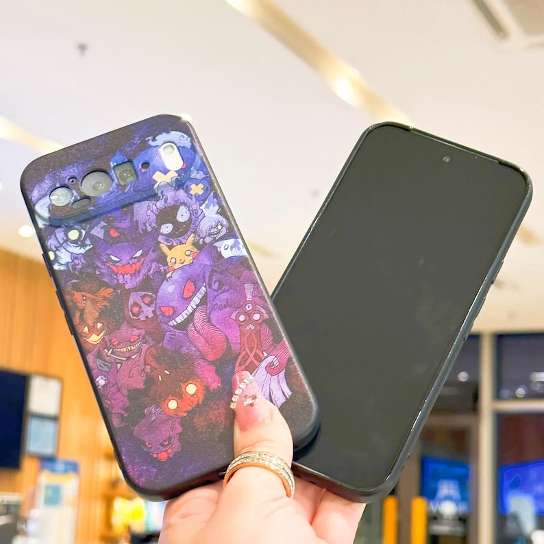 Puede incluir: Una funda negra para smartphone con un dise&ntilde;o colorido de varios personajes de dibujos animados en tonos morados, rojos y azules. La funda se sostiene junto a un smartphone negro.