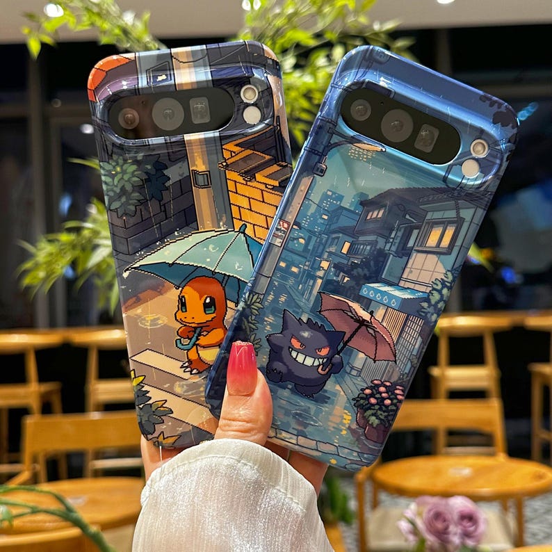 May include: Two phone cases with colorful, pixelated illustrations of Pokemon characters in a rainy cityscape. One case features Charmander under an umbrella, the other Gengar. The cases have a glossy finish and are designed for a smartphone.