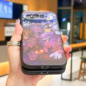 Puede incluir: Funda de tel&eacute;fono negra con un dise&ntilde;o colorido de varios personajes de dibujos animados en tonos morados, rosas y amarillos. La funda tiene un acabado brillante y texturizado. Se muestra en una mano.