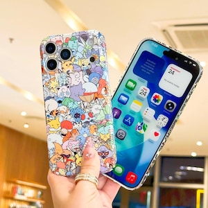 May include: A colorful phone case featuring a pattern of cartoon characters. The case is held next to a smartphone displaying the home screen with app icons and the date, Wednesday 24. The phone case has a clear, glossy finish.