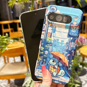 May include: A pixelated phone case featuring a blue and orange Squirtle character holding an umbrella in a rainy street scene. The case has a light blue background with Japanese-style buildings and a pixelated design.