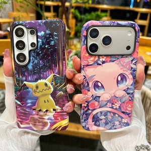 May include: Two rectangular smartphone cases featuring vibrant character illustrations. The left case displays a yellow creature in a dark forest setting. The right case features a pink creature surrounded by pink and blue floral patterns.