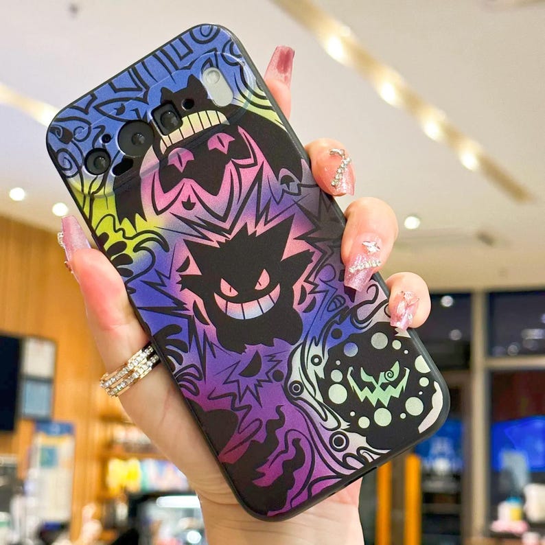 Puede incluir: Funda de tel&eacute;fono negra con un dise&ntilde;o colorido de personajes de dibujos animados en tonos morados, azules, amarillos y verdes. La funda tiene un acabado brillante y se sostiene en una mano.