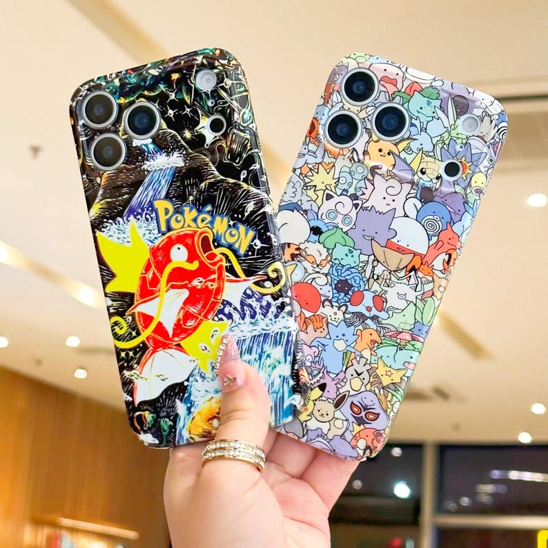 May include: Two phone cases with colorful designs. One case features a red and yellow cartoon character with the word "Pokemon" on a black background. The other case is covered in various cartoon characters in different colors.