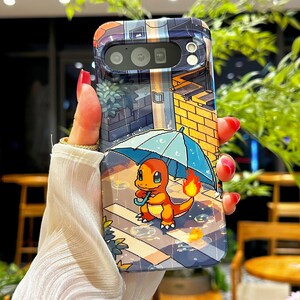 May include: A phone case featuring a pixelated illustration of a Charmander character holding an umbrella in the rain. The case has a colorful design with a cityscape background and is held by a hand with red nail polish.