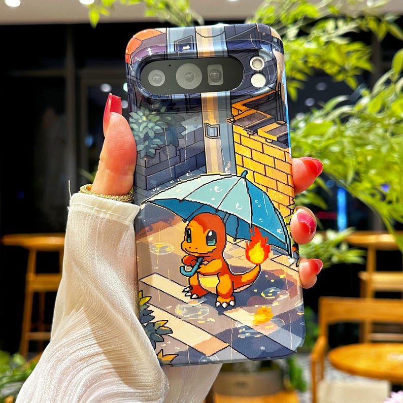 May include: A phone case featuring a pixelated illustration of a Charmander character holding an umbrella in the rain. The case has a colorful design with a cityscape background and is held by a hand with red nail polish.