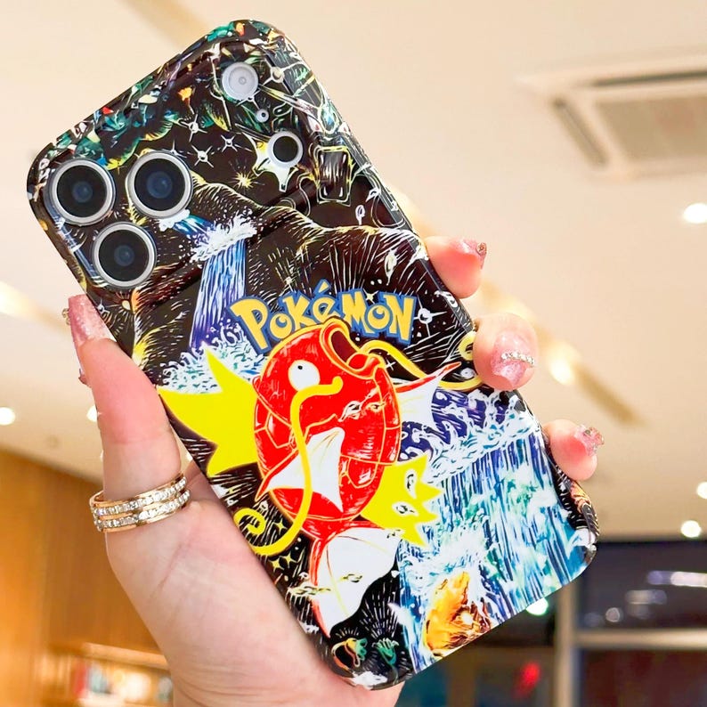 May include: A colorful phone case featuring a vibrant illustration of a red and yellow Pokemon character with the word "Pokemon" in yellow. The case has a black background with a waterfall design and a multi-camera lens.