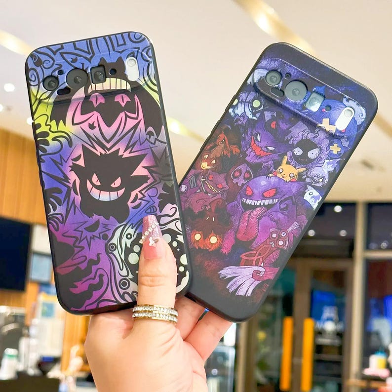 Puede incluir: Dos fundas negras para tel&eacute;fono con dise&ntilde;os coloridos y caricaturescos. Una funda presenta un dise&ntilde;o de Gengar con detalles en morado, amarillo y verde. La otra funda tiene un collage de varios personajes de Pok&eacute;mon en tonos morados y rojos.
