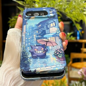 May include: A blue phone case featuring a pixelated illustration of a purple cartoon character holding an umbrella in a rainy street scene. The case has a protective design and a camera cutout.