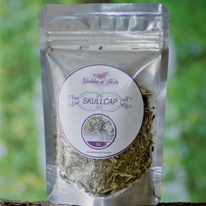 May include: A silver resealable pouch containing dried herbs labeled "Skullcap" with a 1 oz size and the brand name "Goddess of Herbs" printed on a white circle label.
