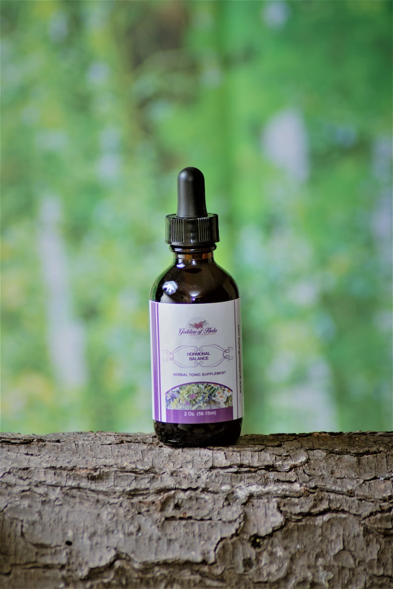 Puede incluir: Una botella de 59,15 ml de suplemento de t&oacute;nico herbal etiquetada como "Goddess of Herbs Hormonal Balance" con un gotero. La botella est&aacute; sobre un tronco de &aacute;rbol.