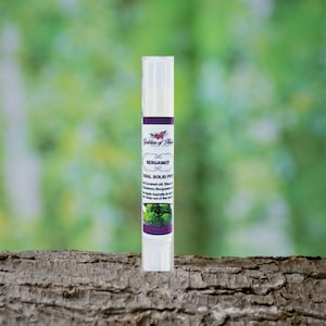 May include: A white tube of bergamot solid perfume with a purple label that says "Goddess of Herbs" and "Bergamot Natural Solid Perfume". The label also includes the ingredients: Coconut oil, Shea butter, Bergamot essential oil. The tube is sitting on a brown tree bark surface.