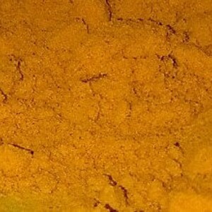 Pode incluir: Close-up de um monte de p&oacute; de a&ccedil;afr&atilde;o-da-terra mo&iacute;do, de uma cor amarelo-alaranjada brilhante. O p&oacute; tem uma textura fina e &eacute; ligeiramente granulado.