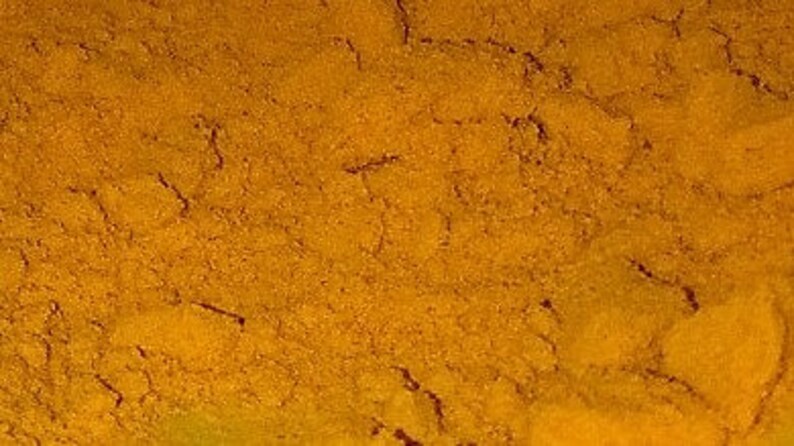 Pode incluir: Close-up de um monte de p&oacute; de a&ccedil;afr&atilde;o-da-terra mo&iacute;do, de uma cor amarelo-alaranjada brilhante. O p&oacute; tem uma textura fina e &eacute; ligeiramente granulado.