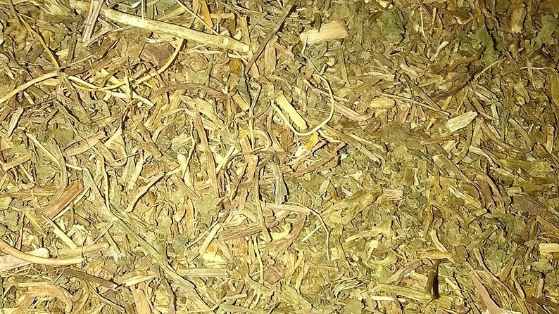 Op de afbeelding: Een close-up van een stapel gedroogde kruiden, voornamelijk bruin en groen van kleur. De kruiden zijn fijn gehakt en lijken een mengsel van verschillende soorten te zijn.