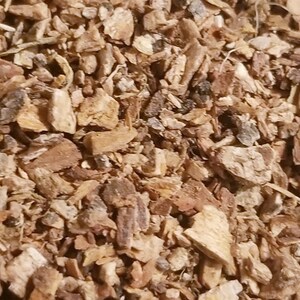 May include: Close-up of a pile of dried, chopped bark pieces. The bark fragments vary in size and shape, with a mix of light brown, tan, and darker brown hues. Some pieces have a rough, textured surface, while others appear smoother. The image suggests a natural, organic material.