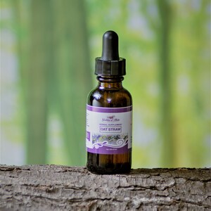 May include: A brown glass bottle with a dropper top, labeled "Goddess of Herbs" and "Herbal Supplement Oat Straw". The bottle is sitting on a piece of tree bark.