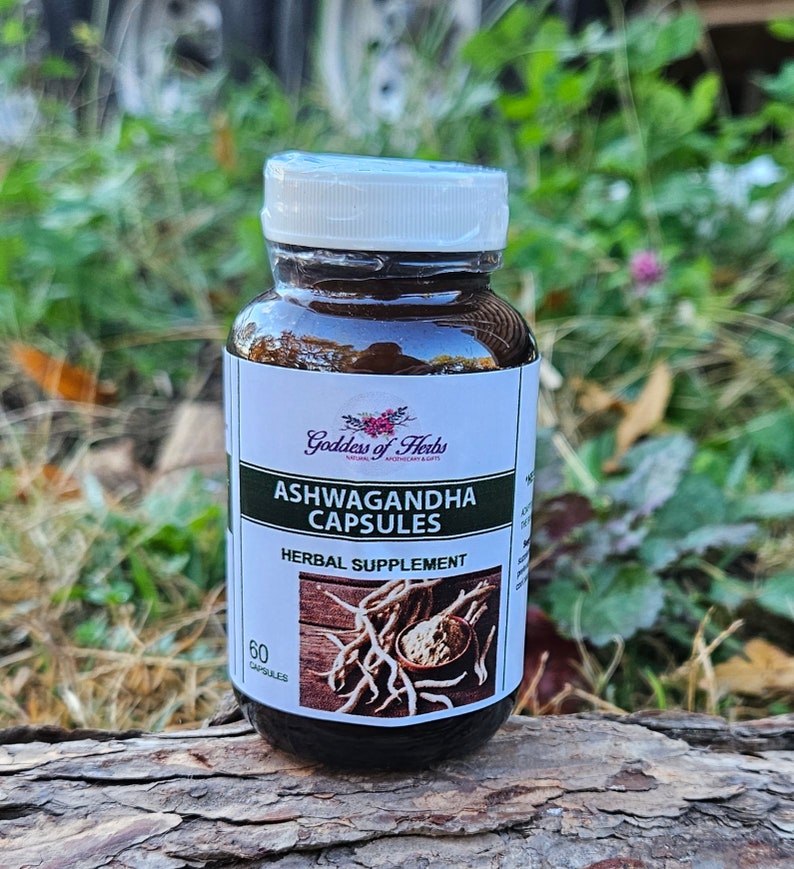 May include: A brown bottle with a white label that says "Goddess of Herbs" and "Ashwagandha Capsules" with a picture of roots and powder. The bottle is labeled as a herbal supplement and contains 60 capsules.