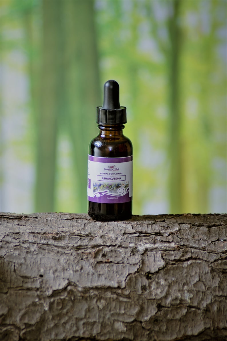 Puede incluir: Una botella de vidrio marr&oacute;n con un gotero, etiquetada "Golden Herbs Herbal Supplement Ashwagandha 1oz (29.57ml)". La botella est&aacute; sentada sobre un trozo de corteza de &aacute;rbol.