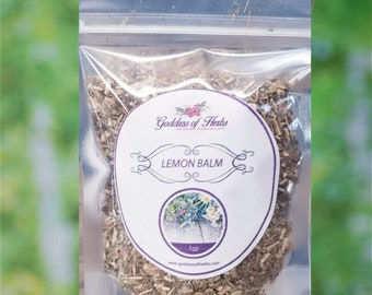 May include: A clear plastic bag filled with dried lemon balm herb. The bag has a white label with the text "Goddess of Herbs" and "Lemon Balm" in a purple circle with a floral design. The label also includes the text "1 oz" and a website address.