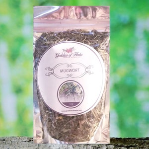 May include: A clear plastic bag filled with dried mugwort herb. The bag has a white label with the text "Goddess of Herbs" and "Mugwort" in black lettering. The label also includes the text "1 oz" and a website address.