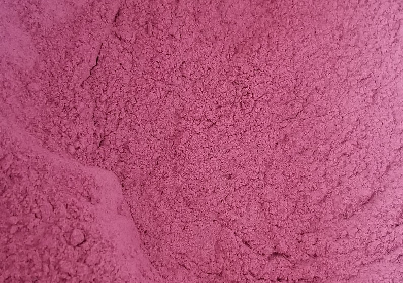 May include: A close-up of a pile of fine, deep pink powder. The powder has a slightly grainy texture and is evenly distributed.