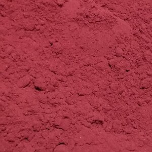 May include: A close-up view of a pile of deep red powder. The powder is fine and smooth, with a slightly grainy texture.