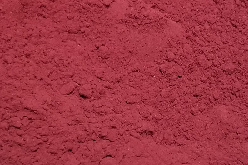 May include: A close-up view of a pile of deep red powder. The powder is fine and smooth, with a slightly grainy texture.