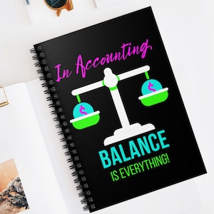 Op de afbeelding: Zwart spiraalgebonden notitieboek met de tekst "In Accounting" in roze script. Het notitieboek bevat een balansweegschaalafbeelding met dollartekens in de pannen en de woorden "BALANCE IS EVERYTHING!" in turquoise.