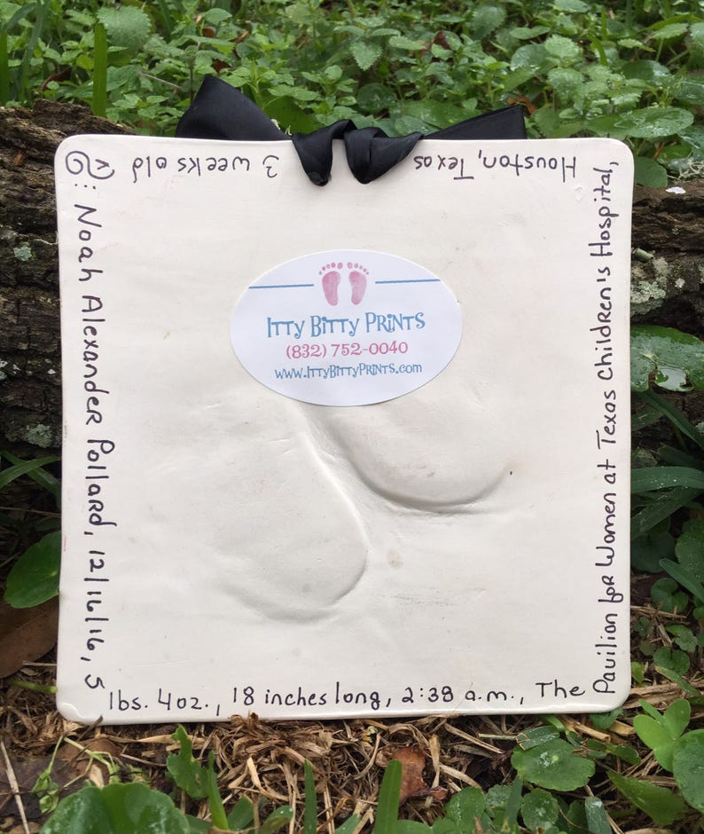May include: White plaster handprint and footprint keepsake with a black ribbon. The inscription reads "Noah Alexander Pollard, 12/16/16, 5 lbs. 4 oz., 18 inches long, 2:38 a.m., The Pavilion for Women at Texas Children's Hospital, Houston, Texas 3 weeks old". The inscription is in black ink. A white sticker with the text "Itty Bitty Prints (832) 752-0040 www.ittybittyprints.com" is in the upper right corner.