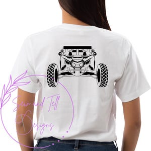 Puede incluir: Camiseta blanca con una silueta negra de un vehículo todoterreno en la parte posterior. El vehículo tiene cuatro ruedas y una jaula antivuelco. El texto "Sew and Tell Designs" está impreso en la parte inferior izquierda de la camiseta.