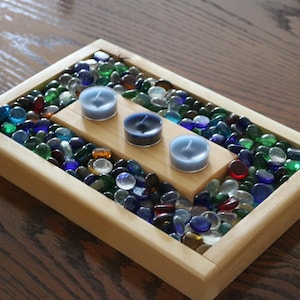 May include: A wooden tray filled with colorful glass stones and three tealight candles. The candles are in a row on a small wooden platform.