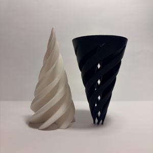 May include: Two spiral-shaped decorative objects. One is cream-coloured, the other black. Both feature a similar design with a twisted, flowing pattern. They are likely decorative items or small sculptures.