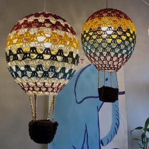 May include: Two crocheted hot air balloon light fixtures hanging from the ceiling. The balloons are multi-colored with red, yellow, white, black, and blue yarn. The balloons have brown crocheted baskets.
