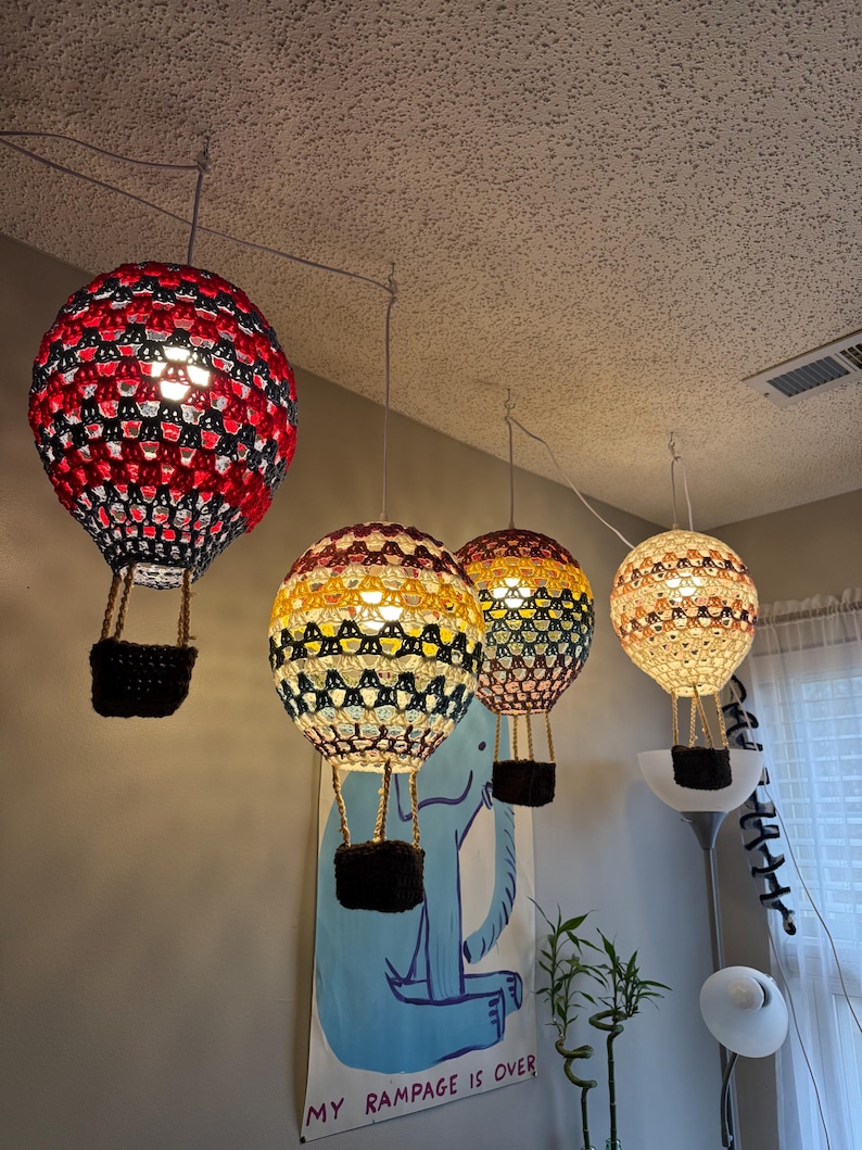 May include: Four crocheted hot air balloon light fixtures hanging from the ceiling. The balloons are red, yellow, blue, and white. The balloons are lit from inside and cast a warm glow. The text "My Rampage is Over" is visible on a blue poster below the balloons.
