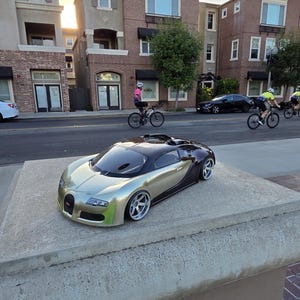 Puede incluir: Un coche a control remoto modelo Bugatti Veyron con un acabado exterior bicolor en oro metálico y negro. El vehículo presenta una carrocería aerodinámica de perfil bajo, ventanas tintadas y llantas plateadas de radios múltiples.