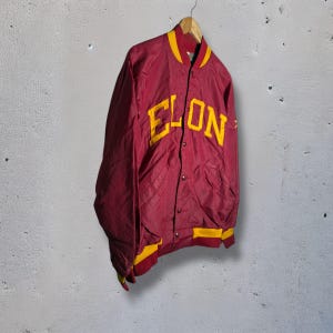 May include: Maroon and gold nylon jacket with the word "ELON" in large yellow letters across the chest. The jacket has a button-up front, yellow trim on the collar, cuffs, and hem, and is hanging on a wooden hanger.