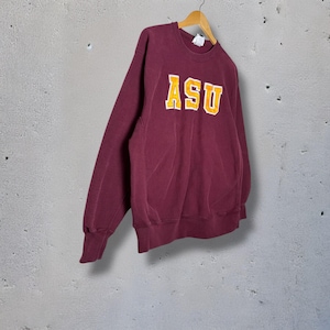 Puede incluir: Sudadera granate con las letras "ASU" en dorado con contorno blanco. La sudadera está colgada de una percha de madera. La tela parece ser un material grueso y suave.