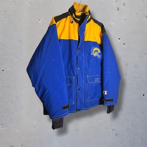 Puede incluir: Chaqueta Champion azul, amarilla y negra con el logo de Los Angeles Rams. La chaqueta tiene cremallera frontal, dos bolsillos delanteros y puños negros. La chaqueta es de estilo vintage.