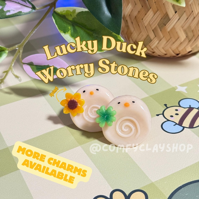 May include: Two Lucky Duck Worry Stones, each with a white base, a spiral design, and a small orange beak. One has a yellow sunflower charm, the other a green clover. The text "Lucky Duck Worry Stones" is displayed.