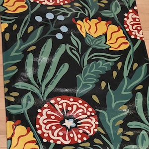 Può includere: Un tappetino da yoga rettangolare con un motivo floreale. Il design presenta grandi fiori rossi e gialli con dettagli bianchi, foglie verdi e bacche blu su sfondo nero. Il tappetino è realizzato in materiale lucido.