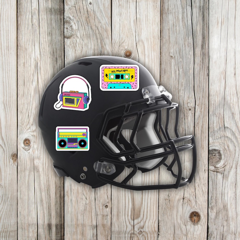 May include: A black football helmet adorned with colorful stickers featuring retro cassette tapes, boomboxes, and a radio with headphones. The stickers have a vibrant 80s aesthetic, with bright pink, yellow, and teal accents.